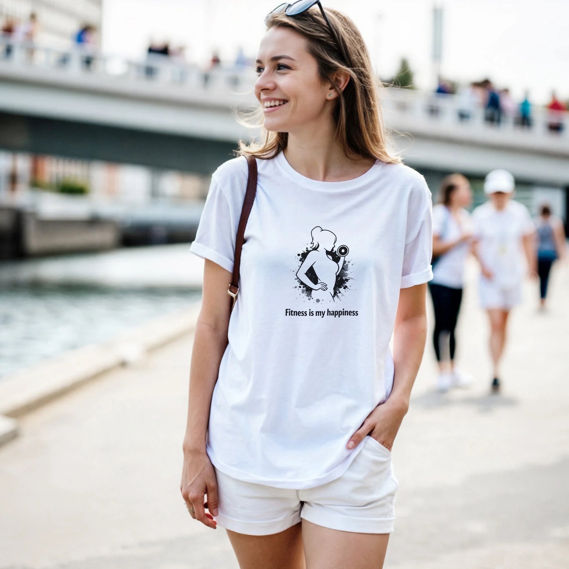 En ung kvinna bär en vit t-shirt med texten 'fitness is my happiness' och visar upp sin styrka vid vattnet.