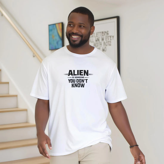 En man bär en vit Alien Urban Graphic T‑shirt med texten 'ALIEN är någon du inte känner'.