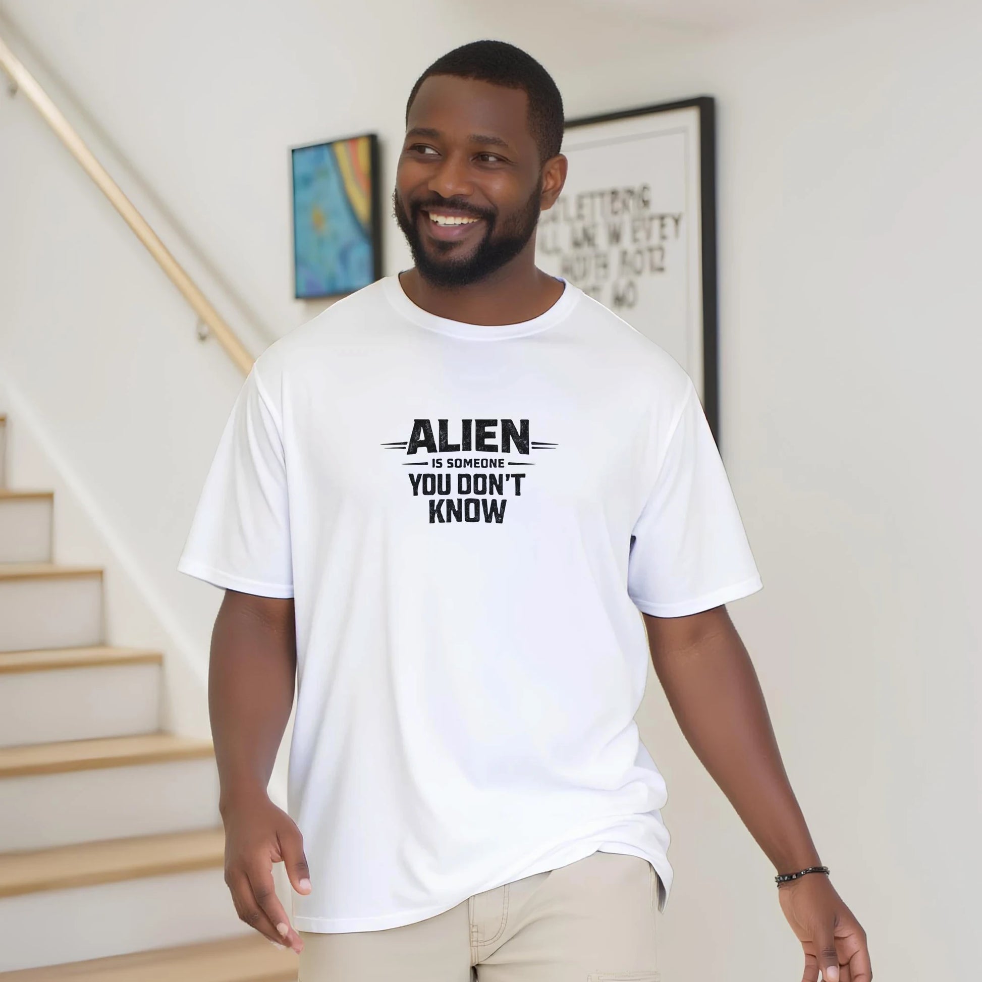 En man bär en vit Alien Urban Graphic T‑shirt med texten 'ALIEN är någon du inte känner'.