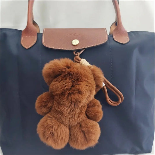 Bag Charm – Mjuk Teddy Nyckelring 18 cm hängande på en elegant väska med bruna detaljer.