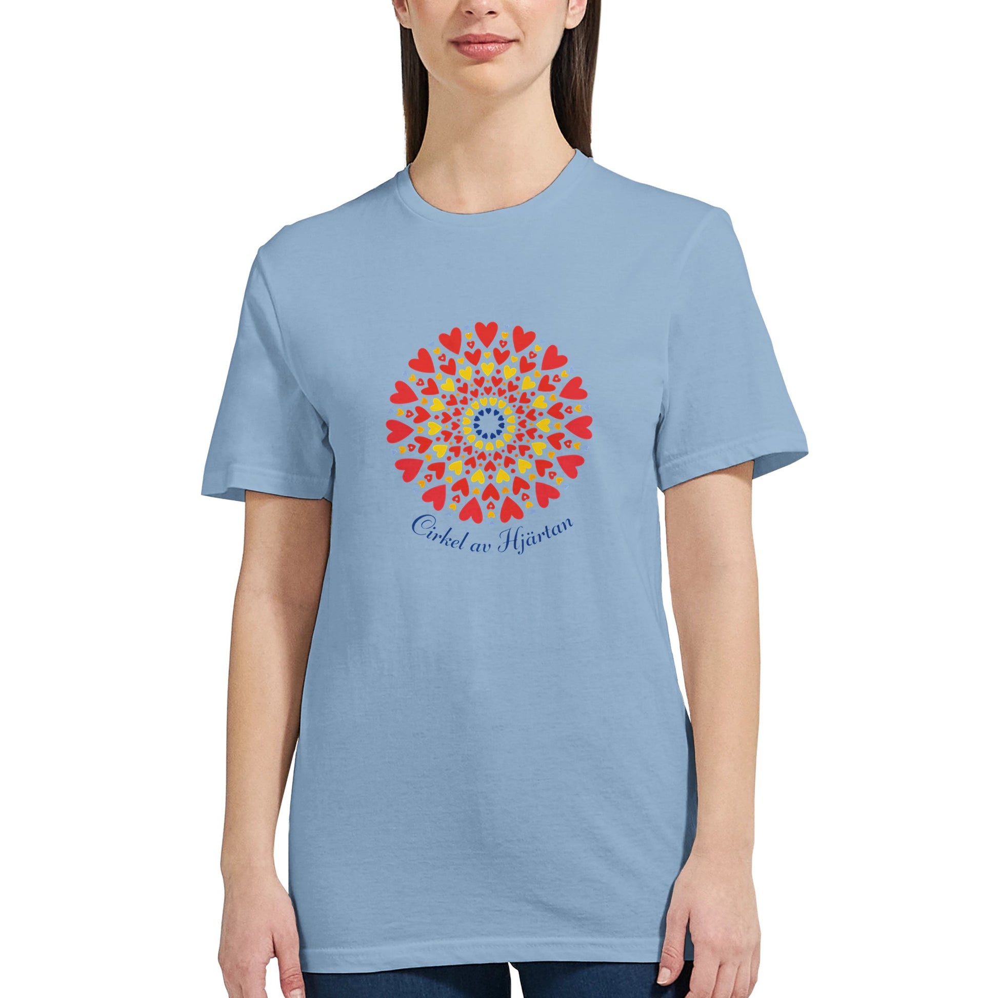 Ljusblå figursydd t‑shirt med ett dekorativt cirkelmönster av hjärtan i gult, rött och blått, samt texten ‘Cirkel av Hjärtan’ under motivet.