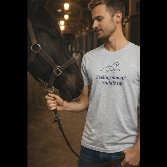 Man som bär Ryttar Tee och står med en häst, med texten "Feeling down? - Saddle up".