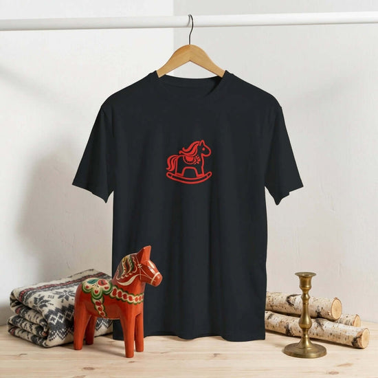 Dalarna Red Rocking Horse T-Shirt displayed on a hanger with a wooden horse figurine beside it.