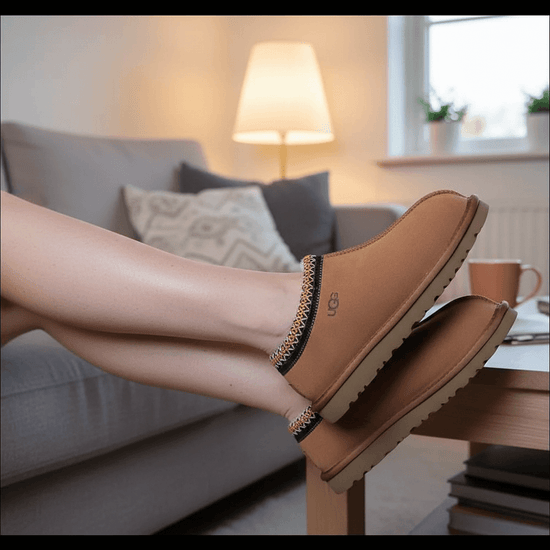 UGG Tasman Chestnut mockatofflor på fötter, perfekta för kalla dagar, som vilar på en soffkant.