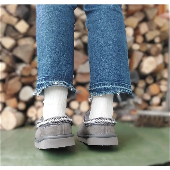 Ugg Tasman II Slipper Mole worn with jeans and white socks, showcasing the stylish design against a wooden backdrop.